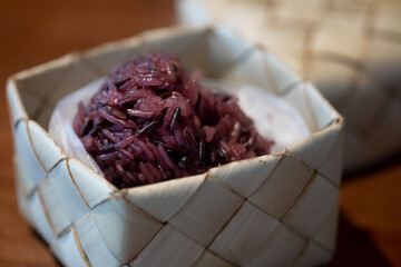 Black sticky rice in woven bamboo rice box on wood table.