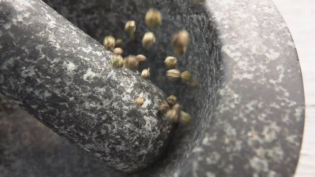Super close-up of green peppercorns falling into the grey stone mortar in slow motion