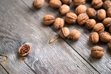 Heap of whole walnuts and one walnut kernel on wooden table - natural pattern background detail. Close up of brown surface texture. Healthy organic food, BIO viands, back to nature concept