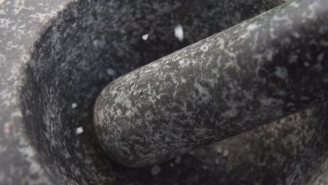 Close-up of the sea salt falling into the grey stone mortar in slow motion