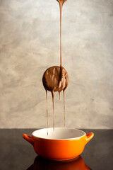 alfajor flying with chocolate falling and bathing. on orange bowl on gray background