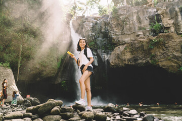Young female traveler standing near waterfall with cellphone
