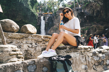 Optimistic female traveler sitting on stones with bottle