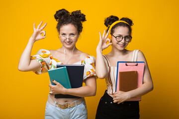 Curly haired twins are gesturing the okay sign wearing glasses with headphones and holding folders...