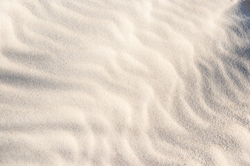 Fototapeta na wymiar Sand background. Shadows and patterns on the sand of dune. Sandy beach for the background. Background, sand, light, beige, wave, reflect, shadow, summer.