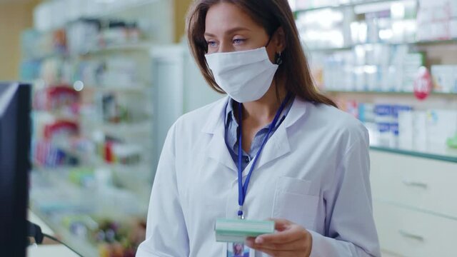 Indoor portrait caucasian young woman pharmacist with protective mask examining drugs in pharmacy center. Medical education. Coronavirus protection. Influenza.