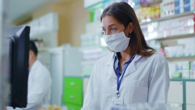Young pharmacist woman in medical mask searching medications by computer surfing database working with male colleague in drugstore. Medicine. Profession. Health concept.