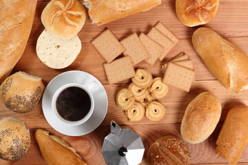 Assorted bread rolls, cookies, coffee cup and moka pot at wooden plank background. Directly Above.