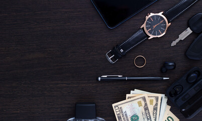 Men's accessories on a dark wooden background . The concept of success and business. Wrist watch, pen, perfume, headphones, ring, car keys, money and phone. Flatlay. Copy space.