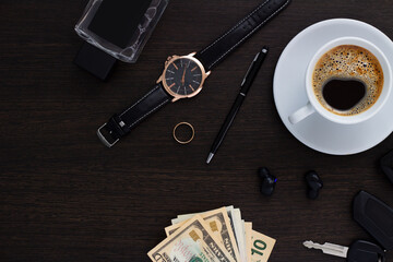 Obraz na płótnie Canvas Men's accessories on a dark wooden background . The concept of success and business. Wrist watch, pen, perfume, headphones, ring, car keys, money and phone. Flatlay. Copy space.