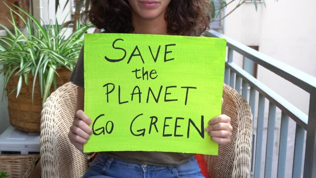 Outdoor portrait of caucasian young woman activist with Save the Planet, World ecology poster - protest demonstration and flash mob on the balcony during Covid-19 Coronavirus quarantine homelockdown  