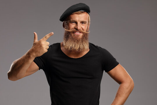 Bearded guy with moustache wearing a black beret hat and pointing