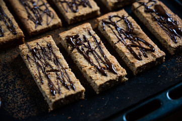 homemade protein müsli bar with banana and oatmeal decorated with dark chocolate as a healthy alternative without sugar, presented on the baking tray, moody photography style
