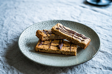 homemade proteein müsli bars with banana and oatmeal decorated with dark chocolate as a healthy alternative without sugar. lie on a rustic plate on a wrinkled linen tablecloth moody photography style