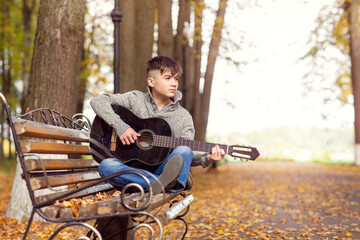 a teenage street musician plays a black acoustic guitar on an autumn day in the Park