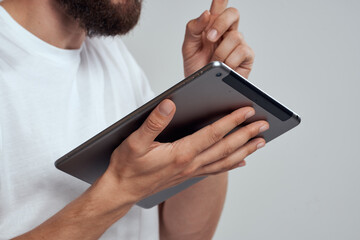 Tablet with a touch screen on a light background male hands white t-shirt cropped view