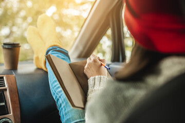 Woman in a car in warm socks is writing notes and plans in a notebook. Cozy autumn weekend trip. Freedom of travel