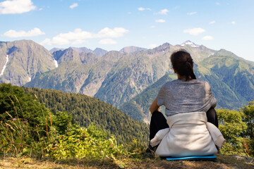 Fototapeta premium Travel, adventure and trekking by Hiking in the mountains. girl is sitting on a scenic peak, looking at the landscape