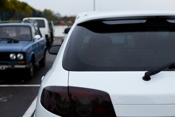 Back window of white car parked on the street in autumn rainy day, rear view. Mock-up for sticker or decals