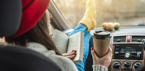 Woman in a car in warm yellow socks is reading a book while sitting in the passenger seat. Cozy autumn weekend trip