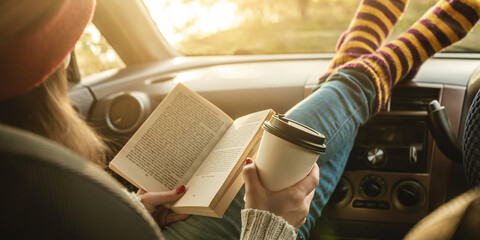 Woman in a car in warm woolen socks yellow is reading a book at sunset. Cozy autumn weekend trip....