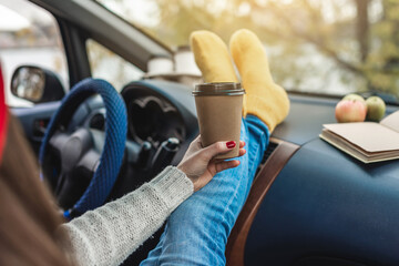 Woman in a car in warm yellow socks is holding a Cup of coffee in hands. Cozy autumn weekend trip. Freedom of travel