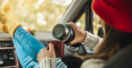 Fototapeta na wymiar Woman in a car in warm yellow socks is pouring coffee from a thermos into a Cup. Cozy autumn weekend trip