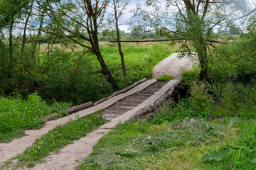 Homemade log bridge over a ditch on a rural road. Summer landscape in the Russian village. Wooden...