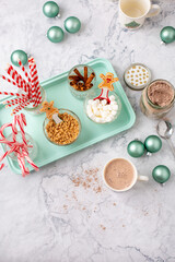 Fototapeta na wymiar Top View of Hot Cocoa Bar with Christmas Cups and Decorations; Multiple Toppings Pictured; White and Gray Countertop
