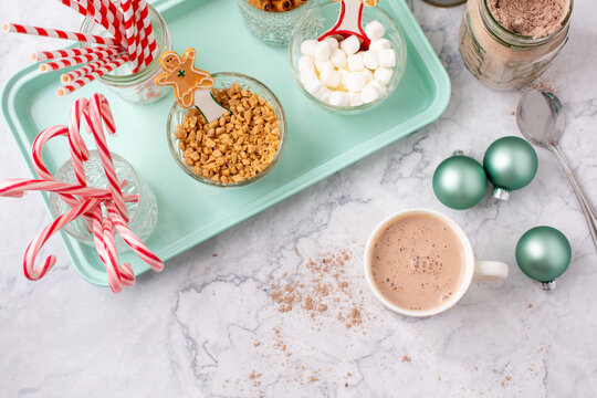 Top View of Hot Cocoa Bar with Christmas Cups and Decorations; Multiple Toppings Pictured; White and Gray Countertop
