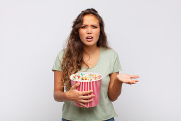 young woman with a pop conrs bucket looking angry, annoyed and frustrated screaming wtf or what’s...