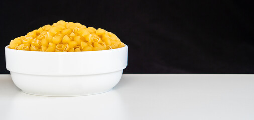 Raw dry uncooked Mini pipe rigate pasta spaghetti noodle on white bowl wooden background for basil...