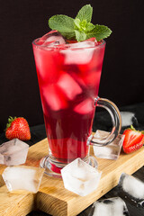 Cold pink lemonade with ice in the glass on the black background. Closeup. Location vertical.