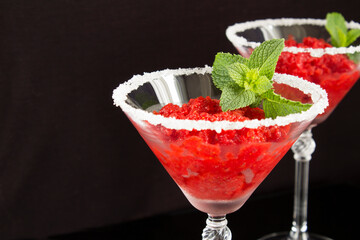 Closeup on frozen juice with strawberry in the martini glasses on the black background
