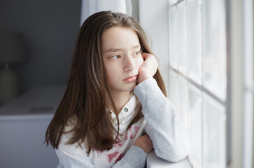 Naklejka premium portrait of a young teenage girl looking out the window with her face against her hand
