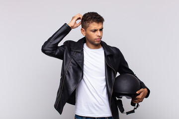 young motorbike rider feeling puzzled and confused, scratching head and looking to the side