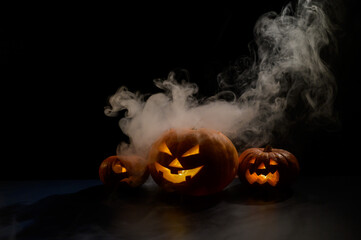 Three creepy halloween steaming pumpkins with a carved luminous smirk on a black background. A...