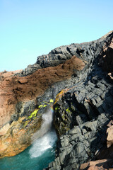The spouting cave spurts water and forms a rainbow on the Isle of Iona, Scotland. Colourful basalt rock surrounds the natural phenomenon and provides a creating and inspiring image.