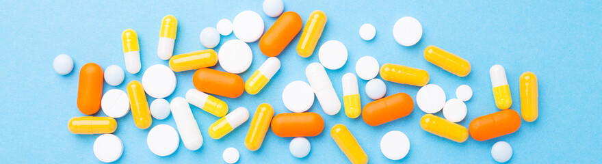 Multicolor tablets and pills capsules on blue background Heap of assorted various medicine tablets and pills. Horizontal banner