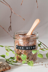 flax seeds in glass jar with wooden spoon and natural elements leaves and bark on grey background