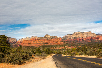 A paved highway passing through a formation of red sandstone rocks and juniper trees outside the city of Sedona, Arizona