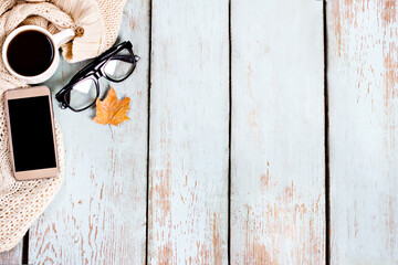 Autumnal composition with pumpkins, leaves, a blanket and coffee on light wooden boards.