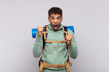 young hiker man shouting aggressively with an angry expression or with fists clenched celebrating success