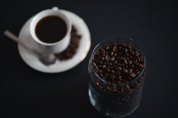freshly roasted coffee beans in the glass container with white coffee cup in the background 