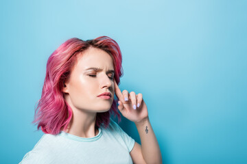 thoughtful young woman with pink hair and tattoo on blue background