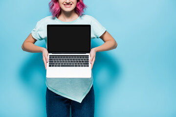 cropped view of young woman with pink hair showing laptop with blank screen on blue background