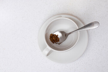 Concept. Empty white ceramic cup and saucer with dry instant coffee on a spoon inside on a beige wooden table