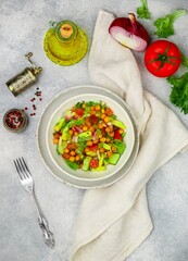 Healthy delicious vegetarian or vegan salad with chickpeas, lettuce, avocado, cucumber, tomatoes, red onion, olive oil and spices. Selective focus, copy space, top view