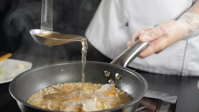Cooking delicious seafood risotto in frying pan. Shot in slow motion. Fish broth being poured out of ladle. Traditional Italian cuisine. Full hd