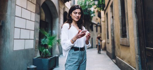 Smiling woman browsing smartphone with coffee in hand
